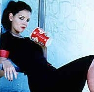 A teenage Katie Holmes as Amanda Hayes, her dyed black hair up in a messy ponytail, knee-length black dress with bright red cuffs on the cap sleeves, fishnet stockings, black fingernail polish, drinking from a Big Gulp with a straw and a skeptical look.