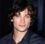 Tom Welling as Clark Kent, curly black hair down past his ears, in a dark blue button up dress shirt, looking older than he did in high school and very handsome.
