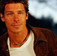Ty Pennington as Jimmy Olsen, short messy brown hair, wearing a white t-shirt and brown jacket, tanned and energetic.