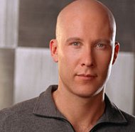 Michael Rosenbaum as Lex Luthor, bald, in a soft grey knit shirt with a zipper and the slightest of smirks, or maybe it's a gentle smile. Only Lex knows.